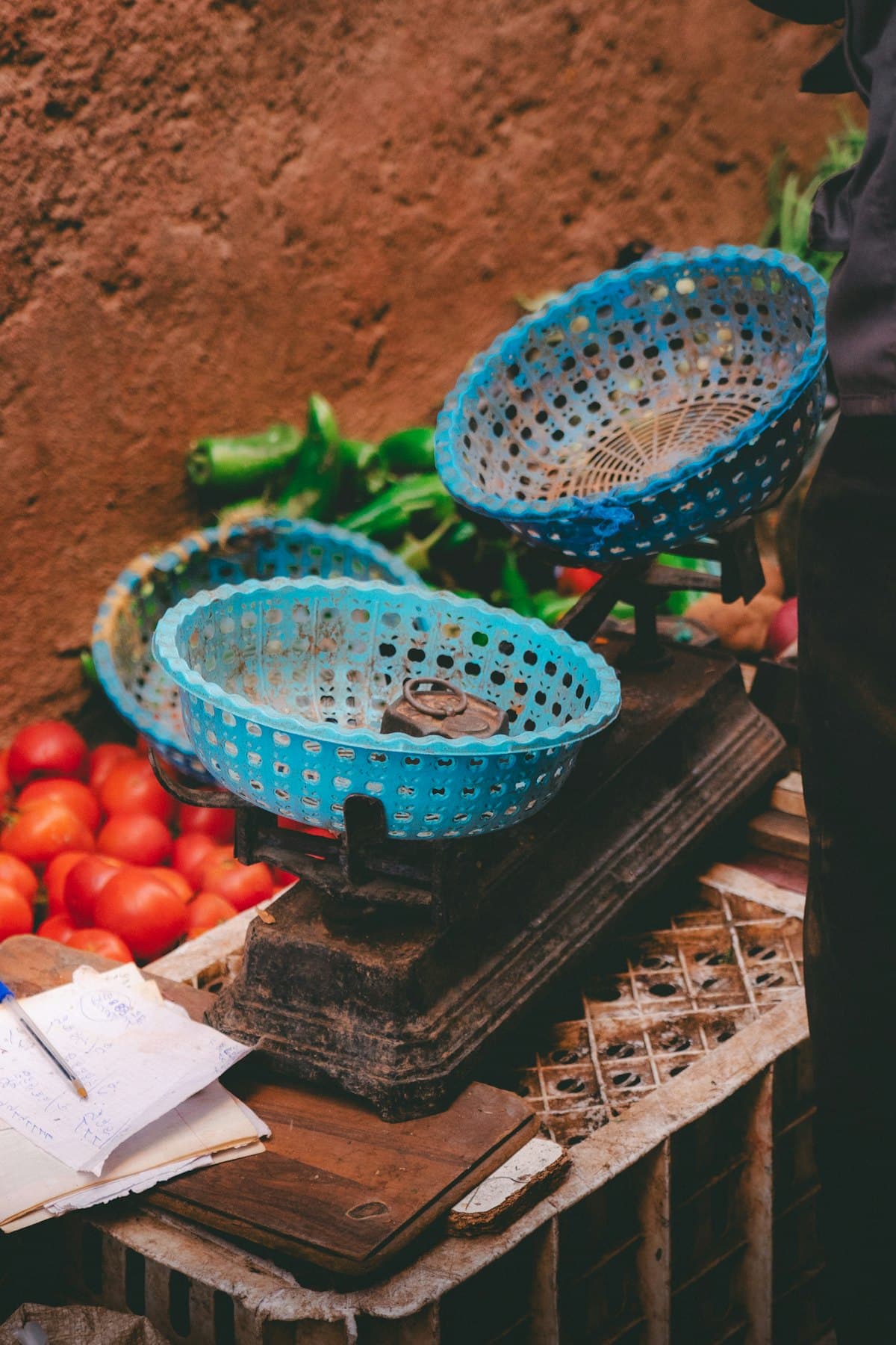 An old two-pan market scale with blue baskets, beside tomatoes and green peppers