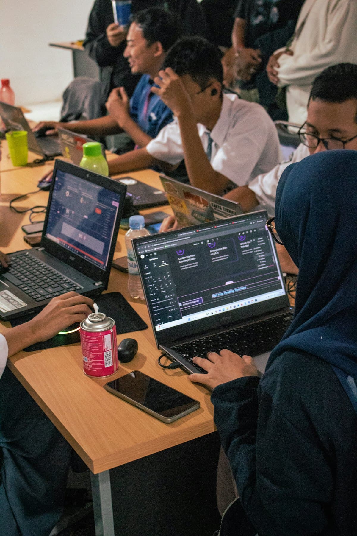 Students working on laptops side by side at a shared desk during a workshop